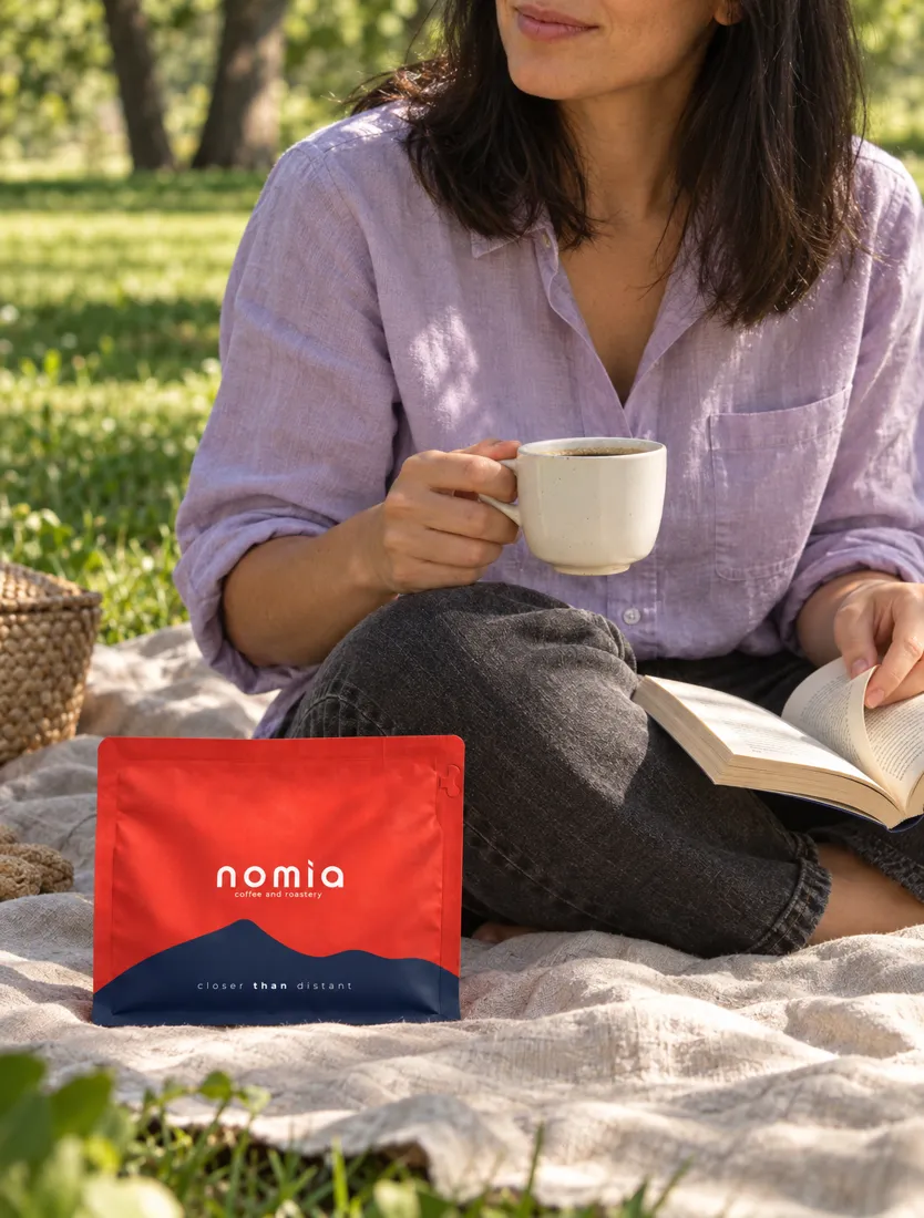 Kitap okurken kahve içen kişi, yanında Nomia paketi